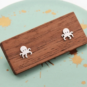 Macro close-up of polished silver octopus stud earrings on a dark wood background
