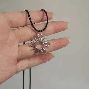 Pendentif soleil argenté avec cordon noir tenu à la main sur fond gris neutre