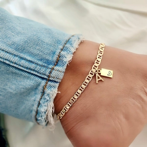 Dettaglio del ciondolo a cuore dorato e della lettera A su una cavigliera alla moda