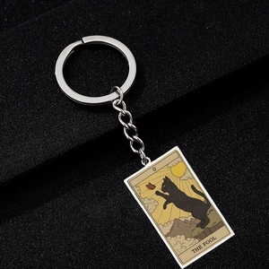 Detail of The Fool tarot cat keychain with black cat and sun on textured background