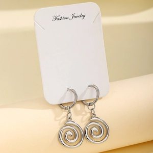 Macro shot of silver spiral swirl pendant earrings on a minimalist jewelry display stand