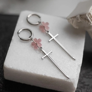 Détail de boucles d'oreilles épée gothique avec fleurs de cerisier roses et anneaux