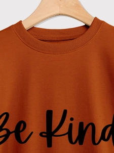 Detail of Be Kind script print and ribbed neckline on a caramel crewneck sweatshirt
