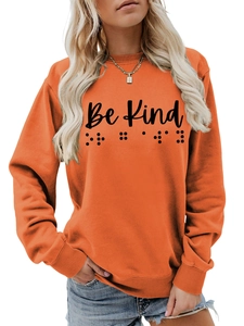 Detail of orange crewneck sweatshirt with Be Kind text and braille dots embroidery