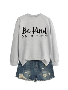 Flat lay of a grey Be Kind sweatshirt with braille dots and blue ripped denim shorts