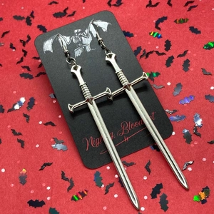Close-up of silver gothic sword earrings on a bat-patterned card with red background