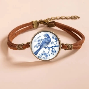 Detail of vintage bronze hummingbird bracelet with blue bird glass pendant and brown cord