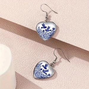 Close-up of heart-shaped blue bird and floral porcelain pattern earrings on steel hooks