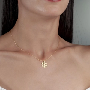 Gros plan d'un collier pendentif flocon de neige doré porté sur le cou d'un modèle