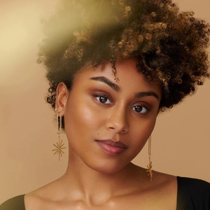 Detail of elegant gold geometric star tassel earrings on a model with soft lighting