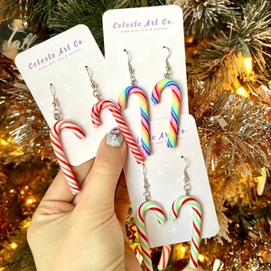 Christmas candy cane earrings in colorful stripes shown against a festive tree background