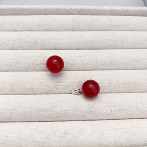 Klassische 10mm rote Achat-Ohrstecker mit Silberstiften auf einer beigen Schmuckablage