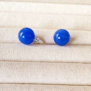 Detail von 12 mm blauen Achat-Ohrsteckern auf einem beigen Schmuckdisplay aus Samt