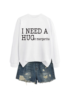 Flat lay of white crewneck sweatshirt with 'I NEED A HUGE MARGARITA' and denim shorts