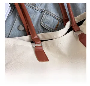 Detail of off-white canvas tote with brown leather handles and 'THE' lettering