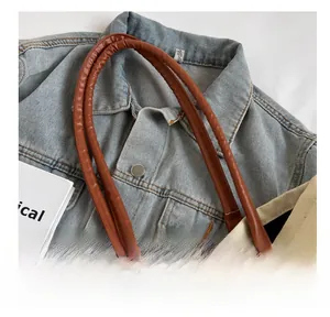 Detail of comfortable brown leather handle on a cream canvas tote bag with metal rings