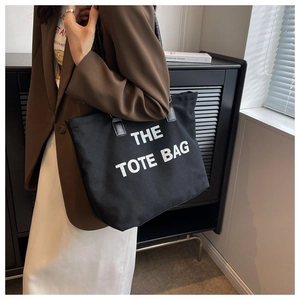 Detail of black canvas tote bag with contrast leather handles and white graphic text
