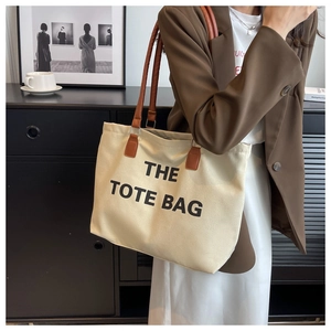 Detail of canvas tote bag with brown leather handles and bold printed text
