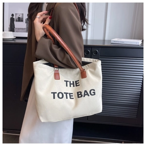 Detail of off-white canvas tote bag with brown leather handles and black printed text