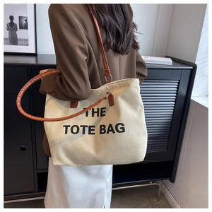 Shoulder view of a cream canvas tote bag with brown leather handles and black text