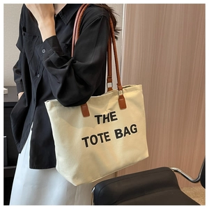 Detailed view of large canvas tote bag with brown leather straps and black printed text