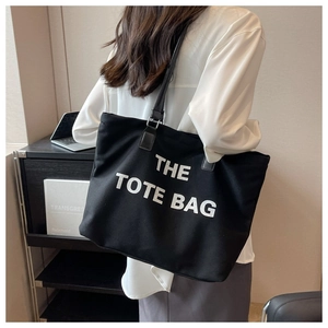 Detail shot of black canvas tote bag with white lettering and leather straps being worn