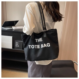 Detail view of large black canvas tote bag featuring white THE TOTE BAG printed text