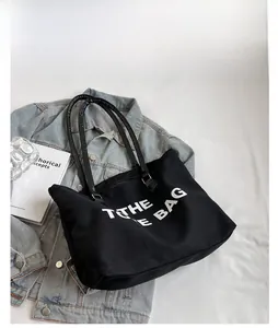 Detail view of black canvas tote bag with white lettering and sturdy leather handles