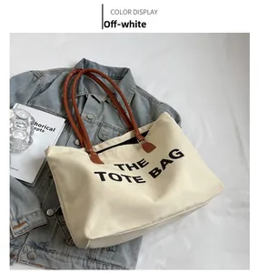 Close-up of beige canvas tote bag with brown leather handles and black typography