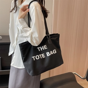Minimalist black canvas tote bag with white lettering carried by a model on shoulder