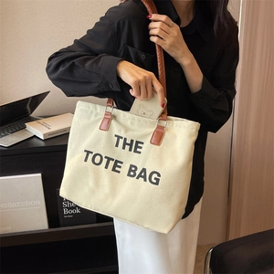 Cream canvas tote bag with brown leather handles showing phone storage capacity