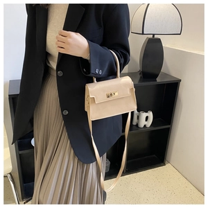 Détail du sac bandoulière en cuir beige avec fermoir doré porté par le modèle