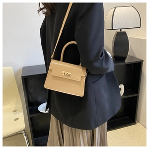 Sac bandoulière beige avec boucle en métal porté par un mannequin dans un intérieur chic