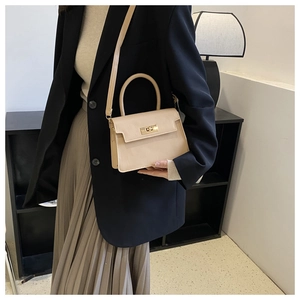 Détail d'un petit sac beige avec fermoir doré tournant et bandoulière sur une veste