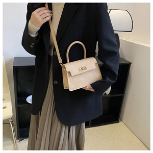 Sac à main trapèze beige en similicuir avec fermoir doré porté par un mannequin