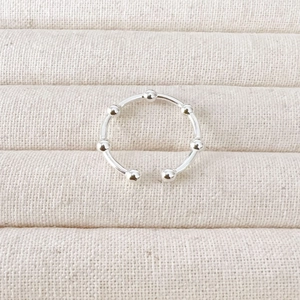 Detailed view of silver bow-shaped ring with small beads on a beige linen background