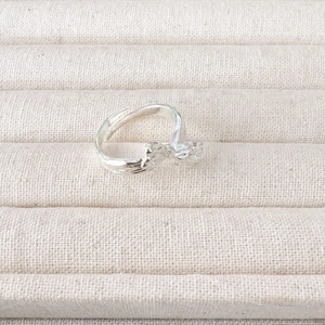 Adjustable silver leaf pattern ring on a beige textured jewelry display tray
