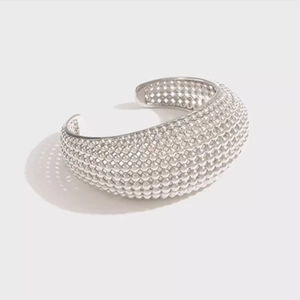 Macro view of silver cuff bracelet with intricate beaded texture and modern industrial design