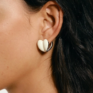 Fashionable cream white heart earrings with silver edges worn by a model in a close-up view