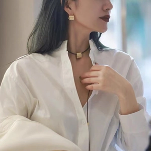 Détail de boucles d'oreilles dorées texturées et pendentif sur cordon cuir