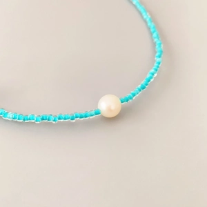 Handmade light blue seed bead necklace featuring a white pearl and a bow-shaped design