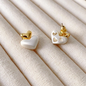 Boucles d'oreilles double cœur dorées et nacrées sur plateau de bijoux en velours