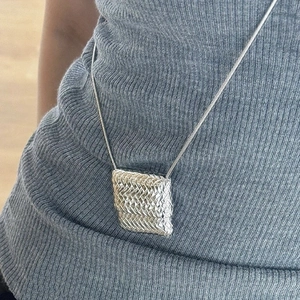 Silberne Halskette mit gewebtem Würfelanhänger an Schlangenkette auf Strickoberteil