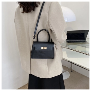 Détail du sac bandoulière en cuir noir avec fermoir doré rotatif et poignée supérieure