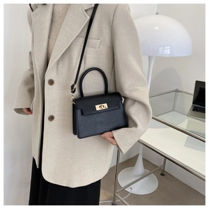 Détail d'un sac à main noir avec fermoir doré porté avec un blazer beige chic