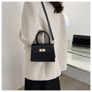 Modèle portant un petit sac carré en cuir noir avec fermoir doré et poignée ronde