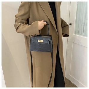 Détail du mini sac bandoulière noir avec fermoir doré sur un trench-coat beige
