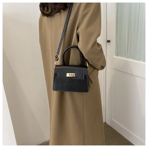 Vue portée d'un sac bandoulière en cuir noir avec boucle dorée sur un manteau beige