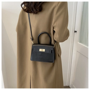 Détail d'un sac à main noir avec fermoir tournant doré porté par un mannequin