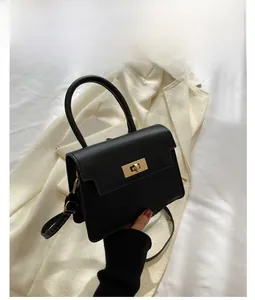 Détail du sac en cuir PU mat noir avec fermoir doré sur un blazer en tweed beige
